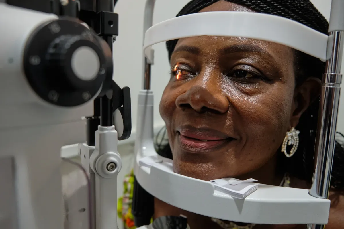 A smiling patient resting her chin on a slit lamp during an eye health examination